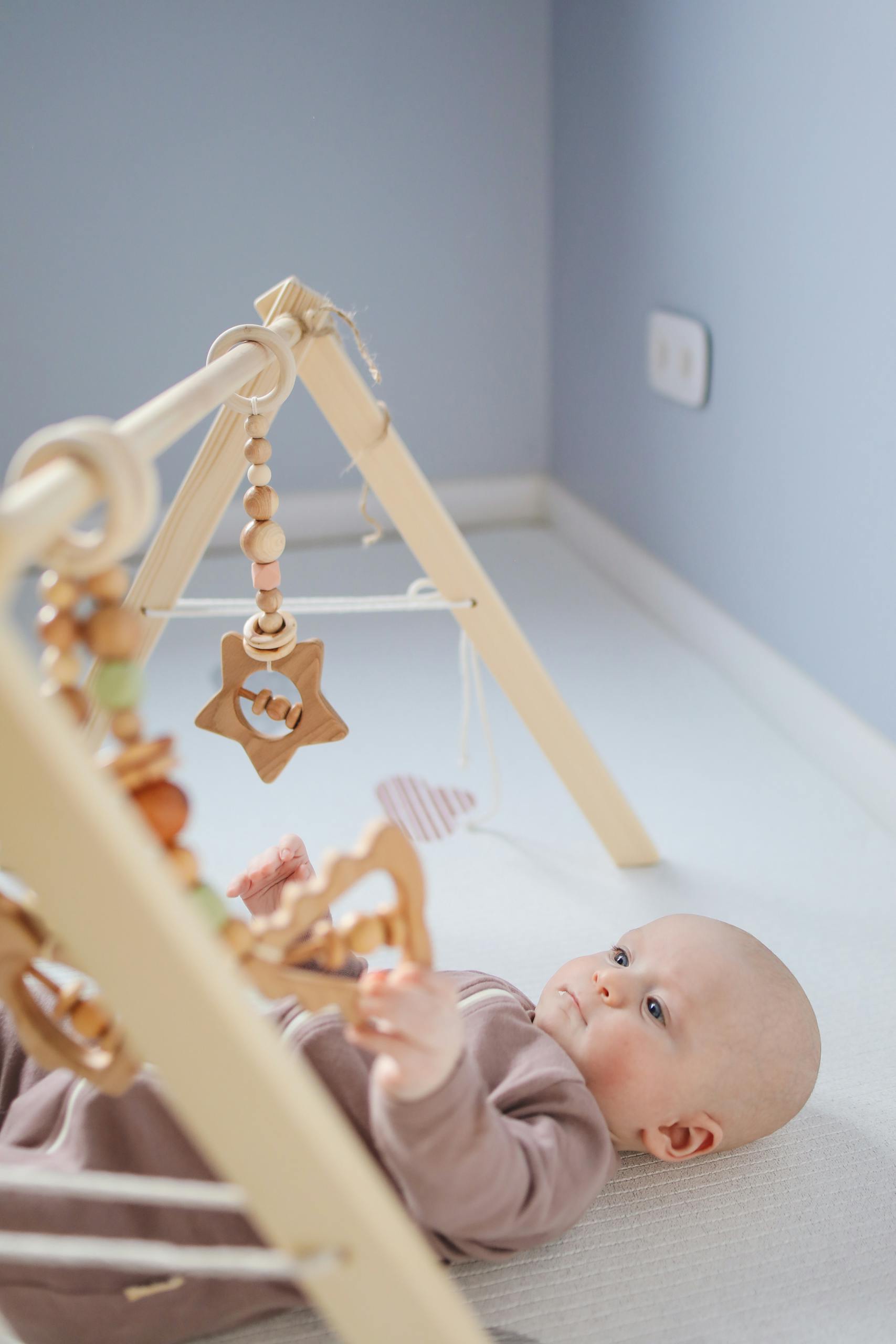 A serene baby lying in a room playing with a wooden toy, creating a peaceful and cozy atmosphere.